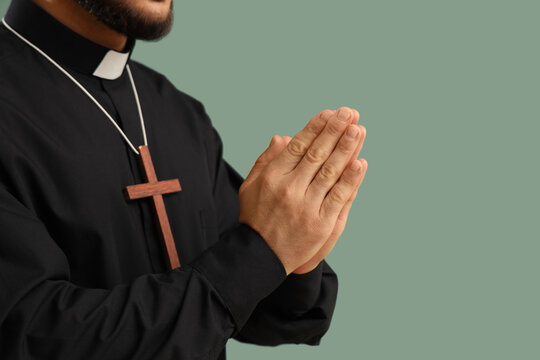 Young priest with wooden cross praying on green background, closeup