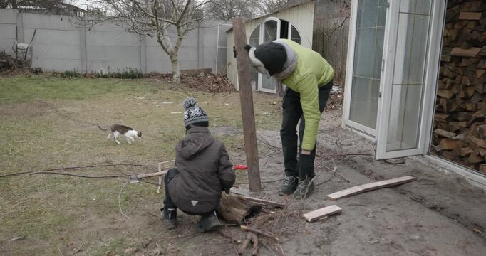 Men with kid cut branches in backyard and stockpile firewood in shed for winter. 4K 10-bit