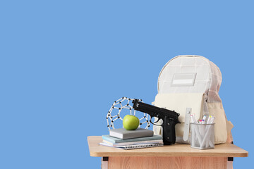 Backpack with gun, apple, books and molecular model on desk against blue background. School...