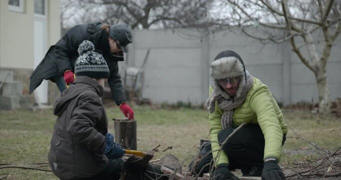 Men with kid cut branches in backyard and stockpile firewood in shed for winter. 4K 10-bit