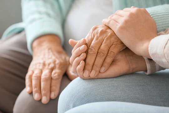 Senior woman with daughter holding hands at home, closeup