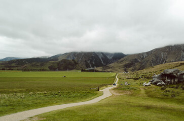 Walking path leading to Castle Hill Kura Tawhiti Conservation Area with mountain landscape under low clouds, Canterbury Region, New Zealand © apiwit