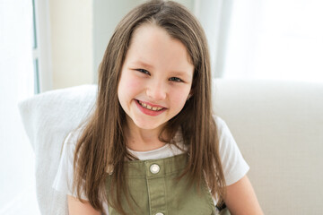 Naklejka premium Happy girl at home. Smiling cute little brown haired Caucasian girl looking at camera. Portrait of happy female child at home. Smiling face of 10 year old girl looking at camera