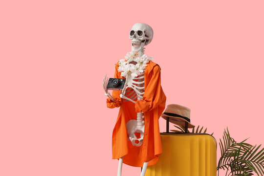 Human skeleton in shirt with photo camera and suitcase on pink background. Travel concept