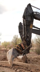 Precyzyjne roboty ziemne koparką gąsienicową: zbliżenie na łyżkę i ramię maszyny budowlanej podczas niwelacji terenu na profesjonalnym placu budowy © tomo81