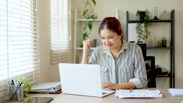 Excited asian office worker winner using laptop computer celebrating goal achievement. getting good news in email raising hands feeling happy  .
