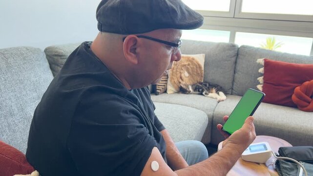 Hombre con parche de gluc&oacute;metro mirando m&oacute;vil pantalla verde
