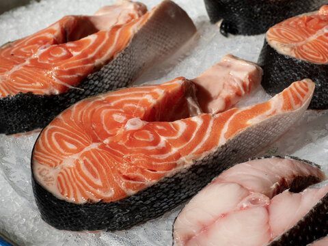 Fresh raw salmon steak with skin and visible texture displayed at fish market on cutting surface in food preparation environment