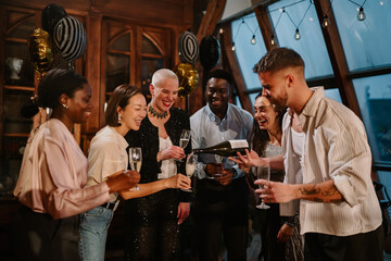 Diverse friends enjoying a celebration, pouring champagne into glasses at an evening party gathering © Zamrznuti tonovi