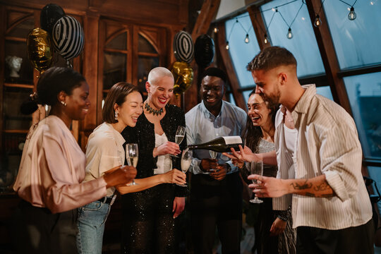 Diverse friends enjoying a celebration, pouring champagne into glasses at an evening party gathering