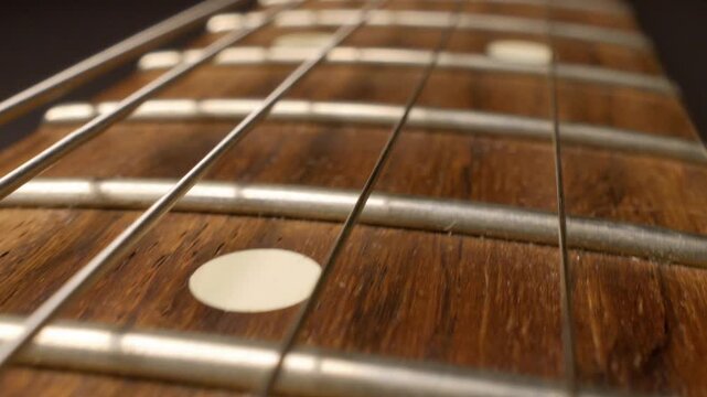 Sliding camera movement along electric guitar fretboard, macro close-up of frets and strings