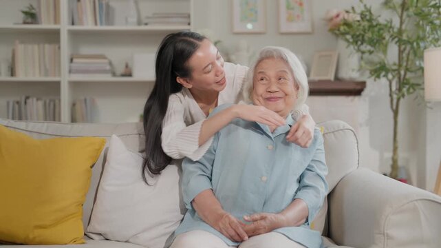 Elderly woman and daughter embrace on sofa in bright living room, smiling warmly with affectionate family home comfort and care scene