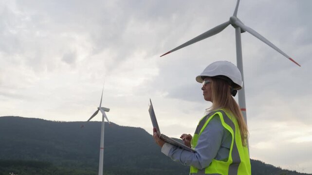A woman engineer stands outdoors with a laptop, monitoring wind turbine performance at a wind farm. The scene highlights innovation, green energy, and the role of women in engineering fields
