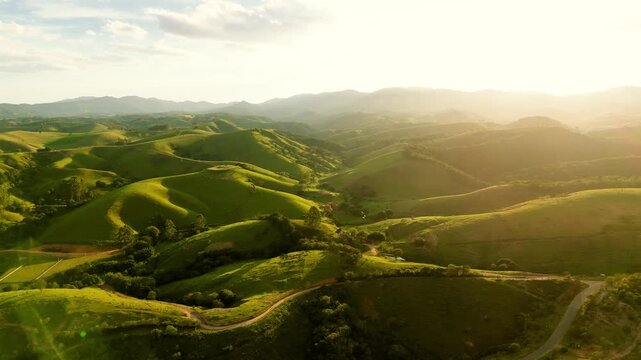 Aerial view of rolling green hills in Mantiqueira mountain range with sunrise backlight and sun flare in Cunha, Brazil. Push in camera movement