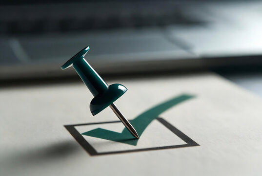 A green push pin is placed in a checkmark box on a white document. It suggests a completed task or selection. The setting is a desk surface with a blurred background.