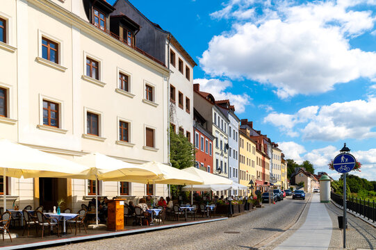 Riverside promenade in Zgorzelec along the Neisse with cafes, umbrellas, colorful facades, cobblestone pavement and blue sky with clouds.