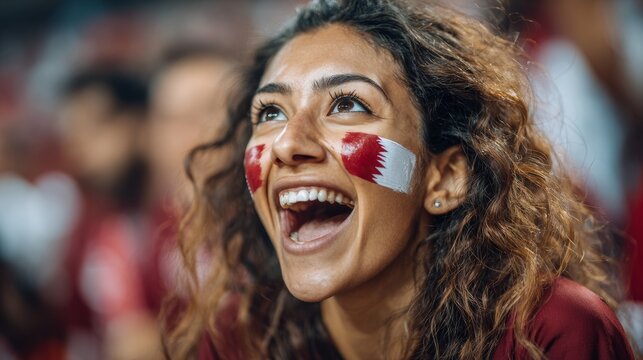 Euphoric woman in a football stadium with her face painted with the colors of the Qatari flag, cheering and supporting her team.