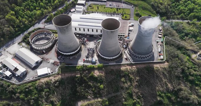 Larderello, Italy - 15 April 2026: Aerial view of Enel Green Power - Centrale Geotermica di Larderello with massive cooling towers emitting steam amidst lush green hills.