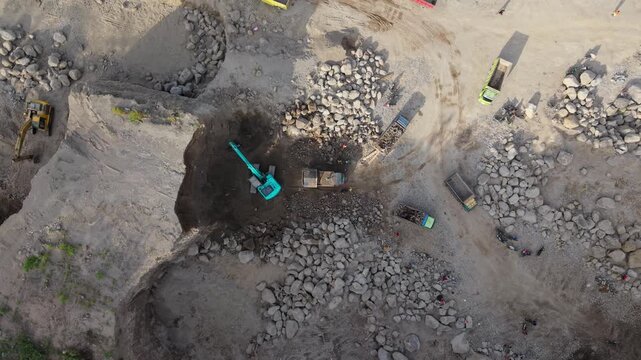 Klaten, Indonesia - 15 April 2026: Aerial view of trucks being loaded by an excavator in a quarry, surrounded by piles of rocks and dusty terrain.
