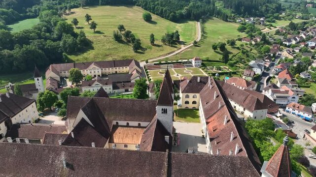 Aerial summer scenery of Sankt Paul im Lavanttal with monastery complex, rooftops, valley landscape, green hills, calm cinematic drone movement, warm atmospheric tones
