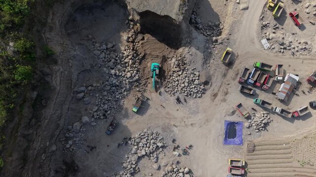 Klaten, Indonesia - 15 April 2026: Aerial view of trucks and an excavator working in a quarry, the scene filled with contrasting earth tones and textures.