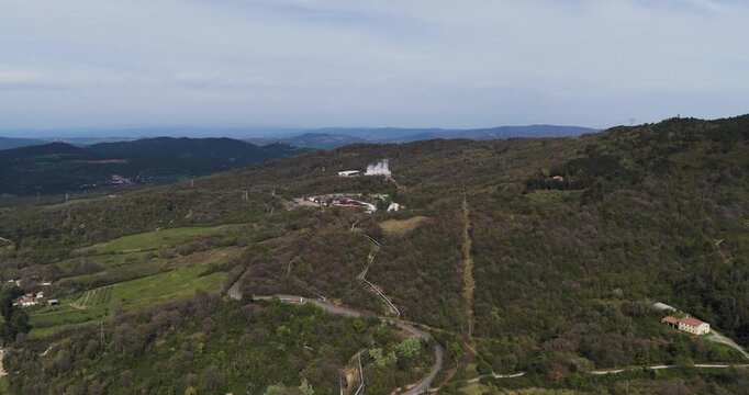 Larderello, Italy - 15 April 2026: Aerial view of Enel Green Power geothermal plant with steam rising from cooling towers surrounded by the forested hills of Tuscany.