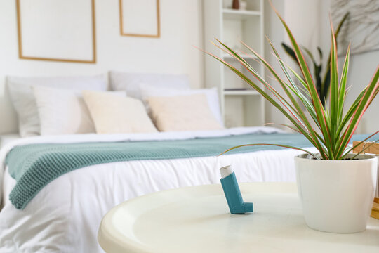Asthma inhaler and plant on table in bedroom, closeup