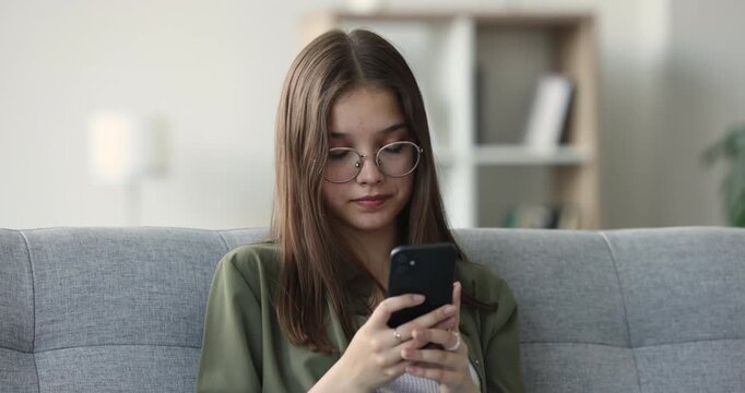 Closeup of Caucasian teen girl checking smartphone, chatting in social media using mobile application sitting on sofa at home. Digital communication, connectivity, life habit, gadget overuse concept