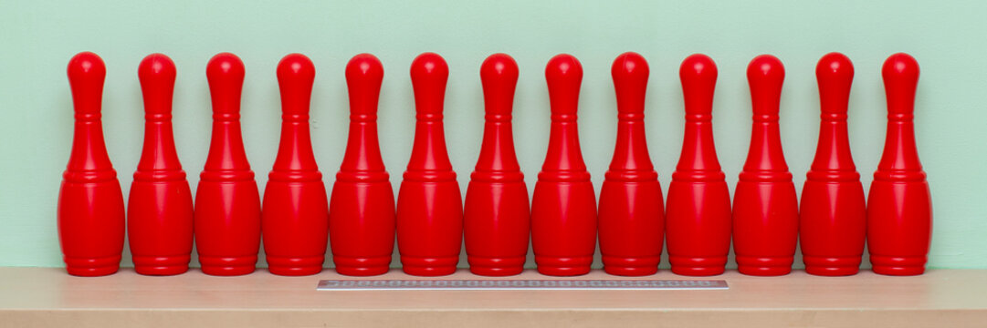 Thirteen red bowling pins standing in perfect alignment on a wooden surface, a ruler emphasizing measurement, uniformity, and precision