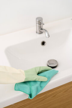 Professional housekeeper in protective gloves wiping white washbasin