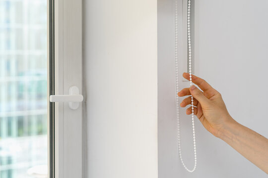Woman adjusts window blinds in living room to control sunlight and shade