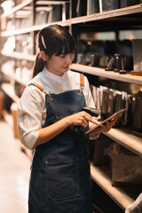 Retail worker in apron using tablet and scanner in store aisle, focused customer service and inventory check © chokniti