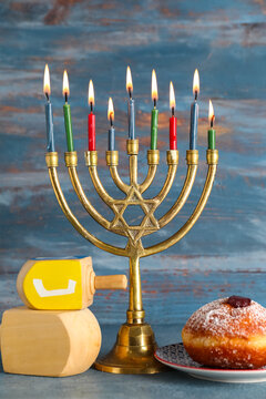 Hanukkah composition with menorah, dreidels and sufganiyot on blue wooden background