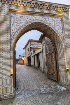 Ornate archway and carved wooden gate on  historic Zarqaynar Street leading to narrow streets and old houses and courtyards surrounded by clay walls in Tashkent old town