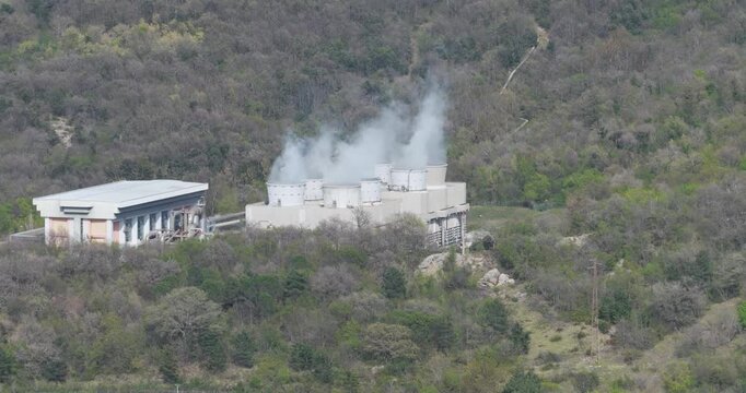 Larderello, Italy - 15 April 2026: Aerial view of Enel Green Power geothermal plant with steam rising from cooling towers nestled in the forested hills of Tuscany.