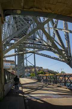 Porto, Portugal - 13 July 2021: View of the Dom Luis I Bridge's intricate metal latticework against the clear sky, as pedestrians stroll along the sunlit upper deck..