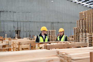 Naklejka premium Two Workers in Yellow Hard Hats and Neon Vests Inspect Wooden Pallets During Warehouse Quality Control Assessment in a Large, Dimly Lit Industrial Facility.