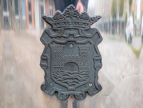 Ponferrada, Leon, Spain; 01-18-2026: Macro view of the Ponferrada coat of arms created with a dark, high-relief material, screwed onto a reflective waste bin