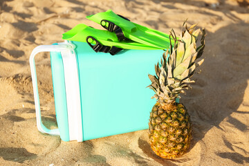 Beach cooler, flippers and pineapple on sand © Pixel-Shot