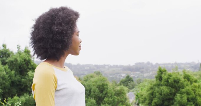 African American woman spotting camera, turning on hilltop, wearing yellow raglan shirt, laughing