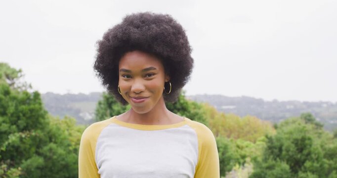 Woman facing camera smiling, laughing with joy on hill in yellow raglan sleeves and gold hoops