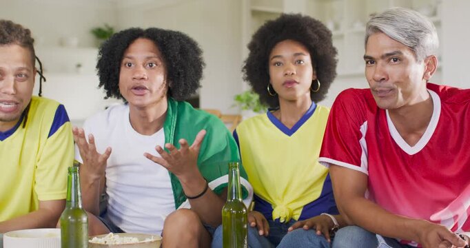 Vertical video: Diverse friends watching match on sofa at home, reacting to tv play while snacking