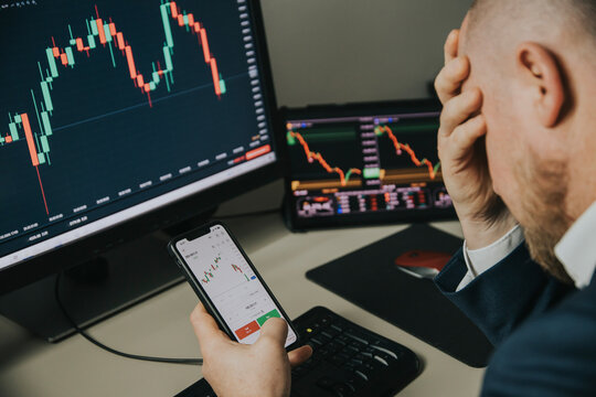Stressfull trader holding smartphone, using trading app with stock market charts for financial analysis and monitoring investment data.