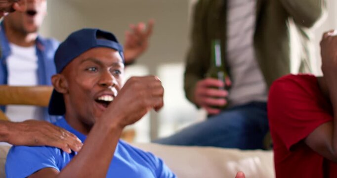 Diverse men cheering after adult African American man in blue cap scoring, holding white controller