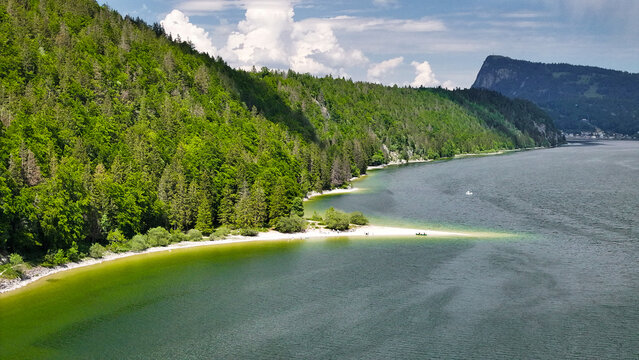 Aerial view of the turquoise waters meet the emerald forests surrounding Lac de Joux, revealing a serene sandbar, Le Lieu, Vaud, Switzerland.