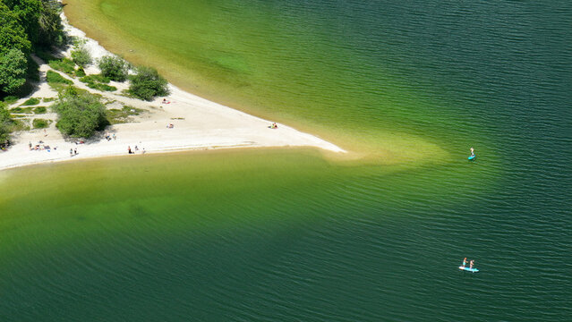 Aerial view of the sandy beach meeting the serene waters of Lac de Joux, creating a tranquil oasis under the sun, Le Lieu, Vaud, Switzerland.