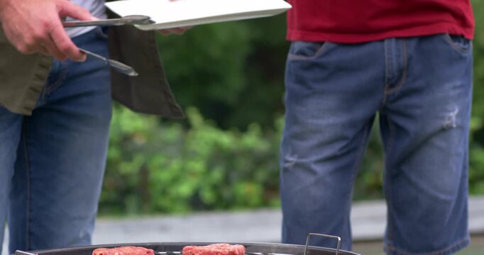 Vertical video: Reaching plate, cook pausing tongs, plating patties at BBQ, guest holding bottles