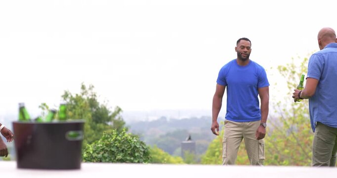 African American men gathering, man in blue approaching right man with green bottle at picnic table