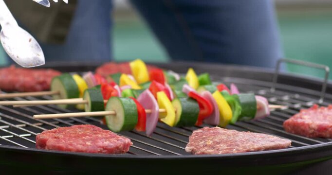 Vertical video: Lifting tongs aproned cook nudging kebabs pressing patties in yard to cook evenly