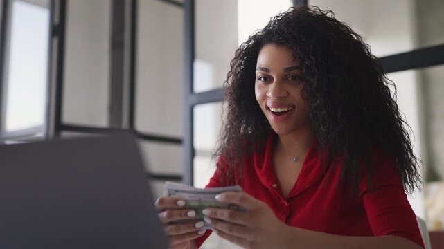 Joyful Black woman developer counting money, happy with startup earnings